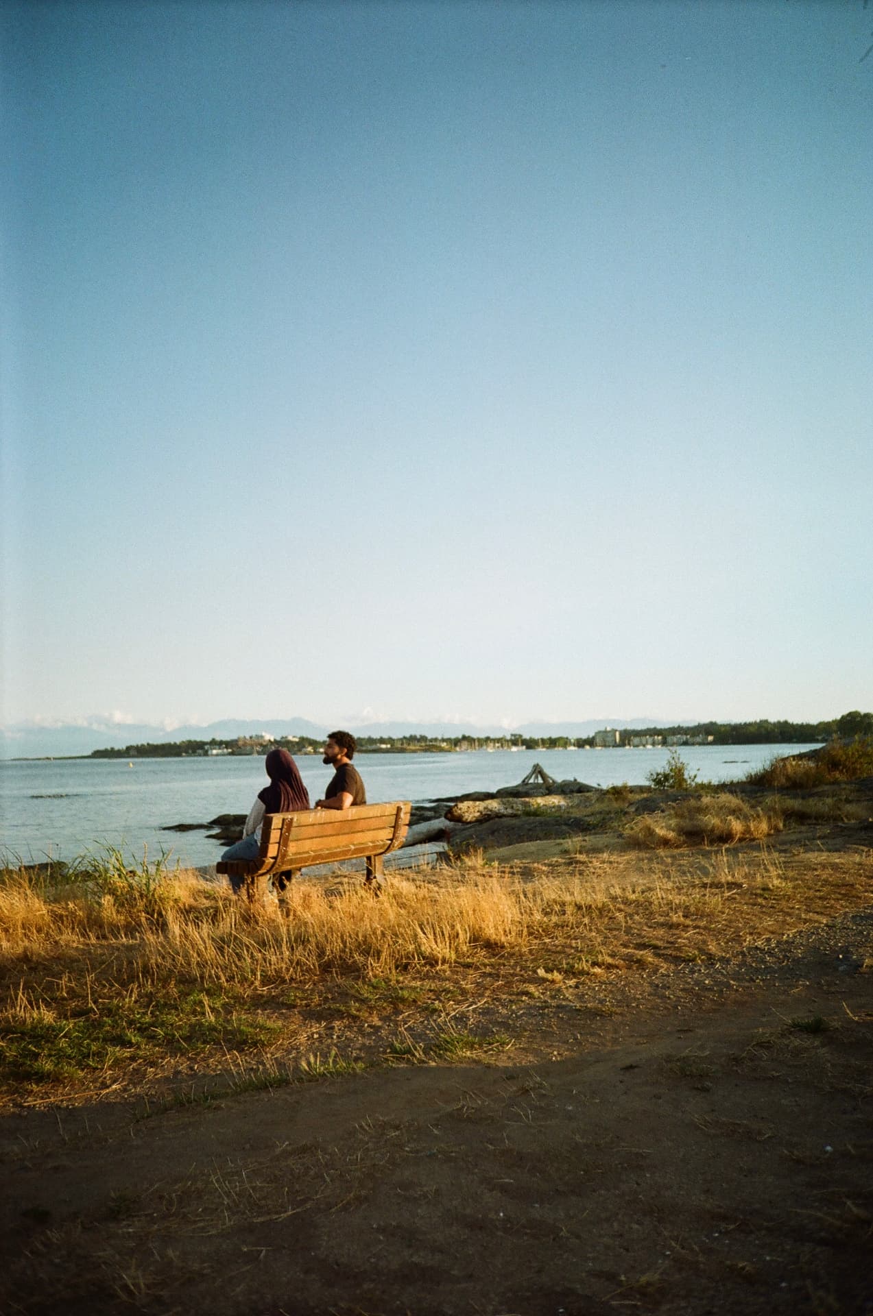 Two people on a bench looking out over the water at golden hour